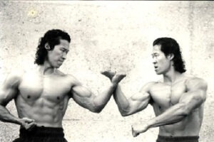 Two muscular martial artists engaging in a powerful arm-to-arm block, capturing the intense physical conditioning required for taekwondo mastery and cinematic reelstunt action.